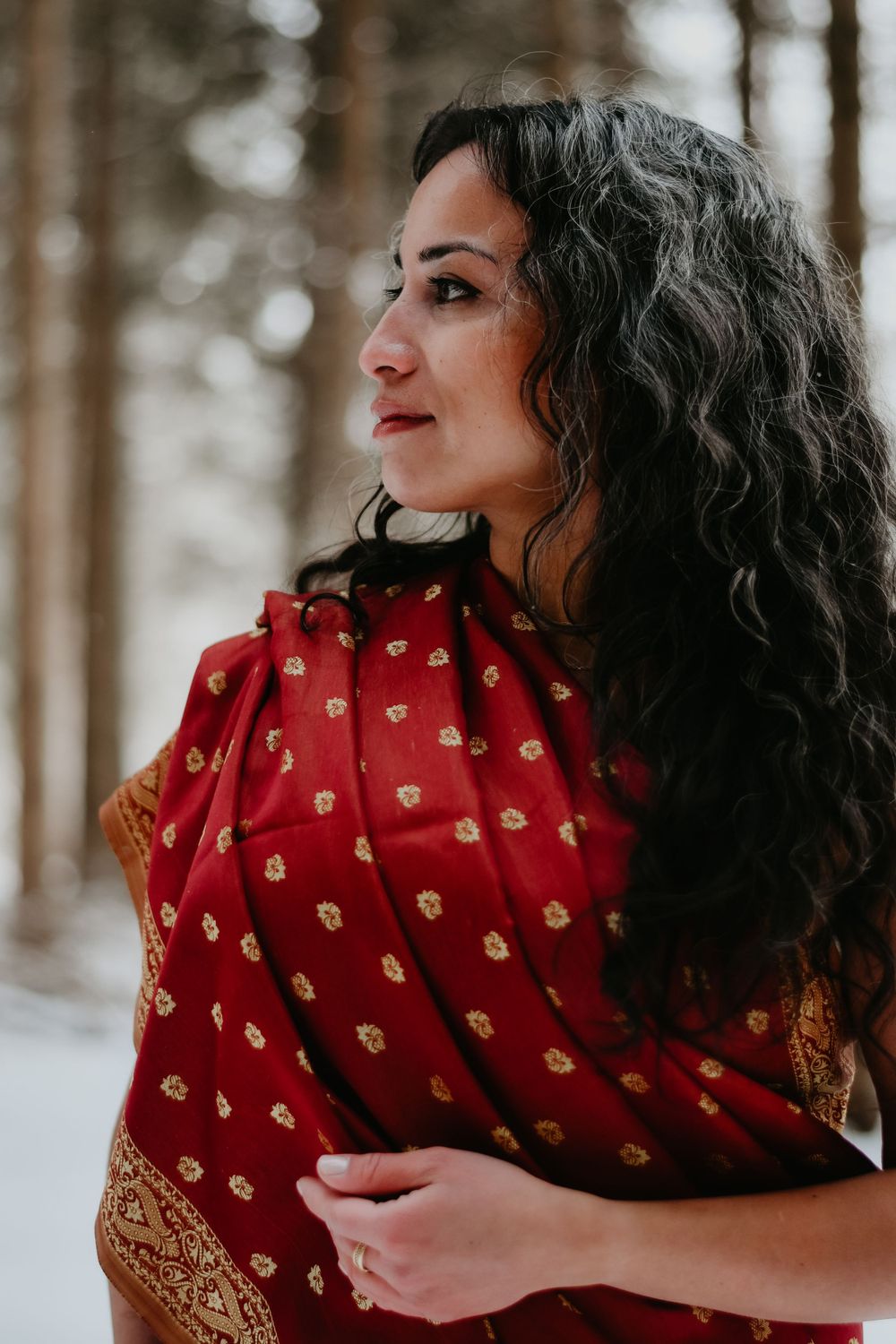 Side profile portrait wearing red patterned shawl in winter forest setting.