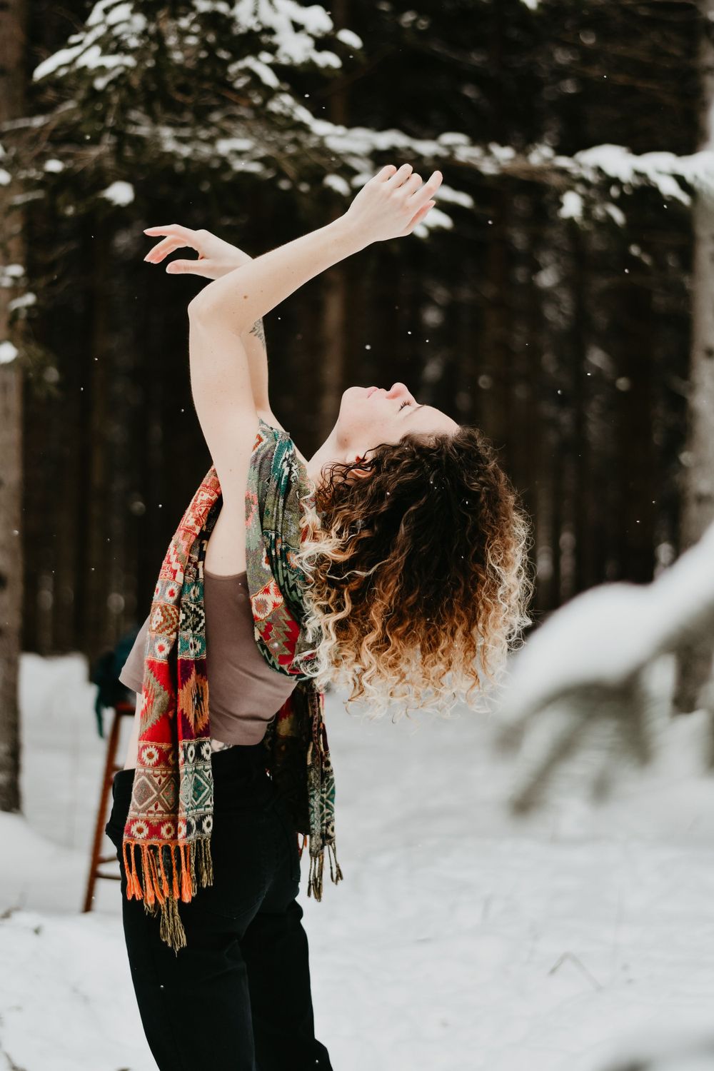 Person in colorful scarf dances joyfully in a snowy forest setting.