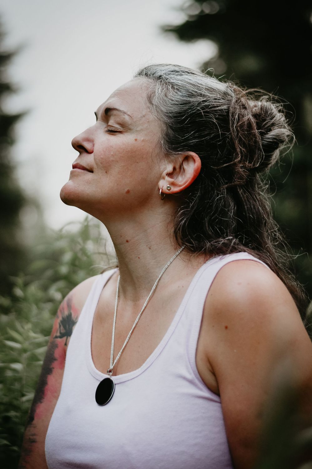 A person enjoys a peaceful moment outdoors wearing a white tank top and silver pendant necklace.