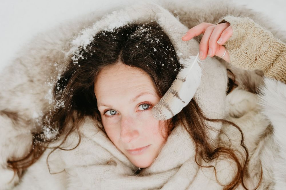 Winter portrait of someone lying in cozy blankets with snow in their curly hair.