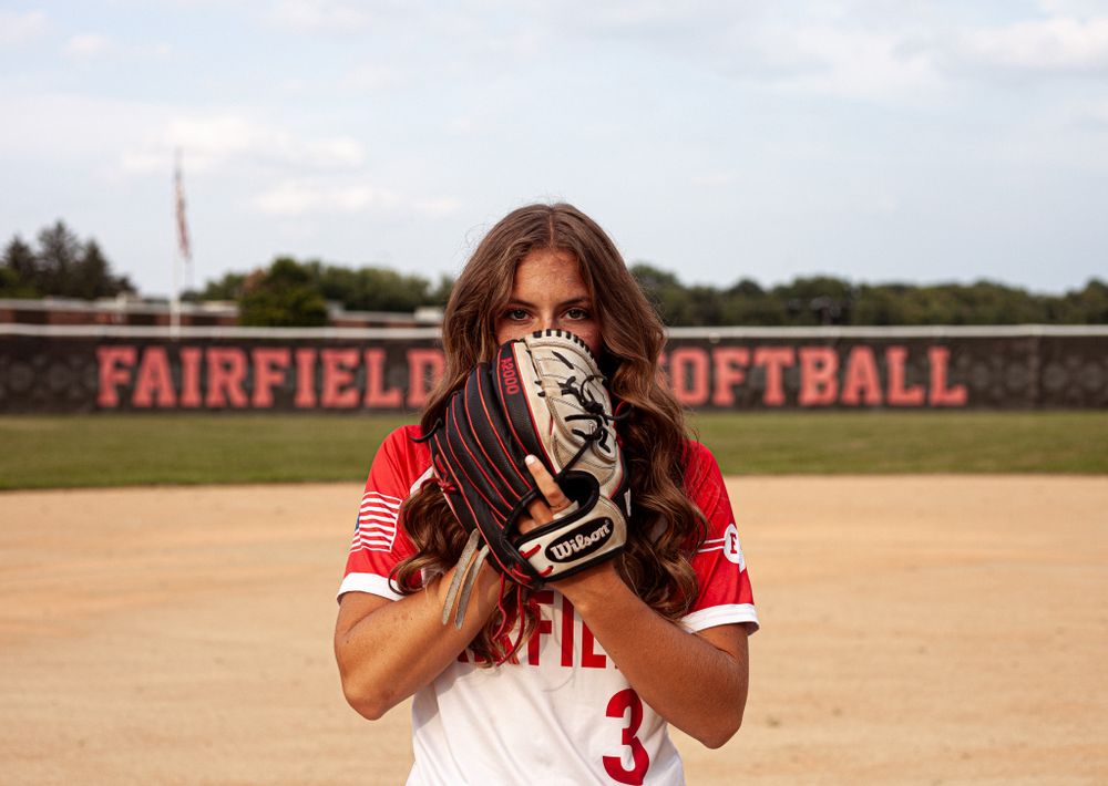 A female softball player holds a glove over her face at Fairfield Softball field wearing jersey number 3.