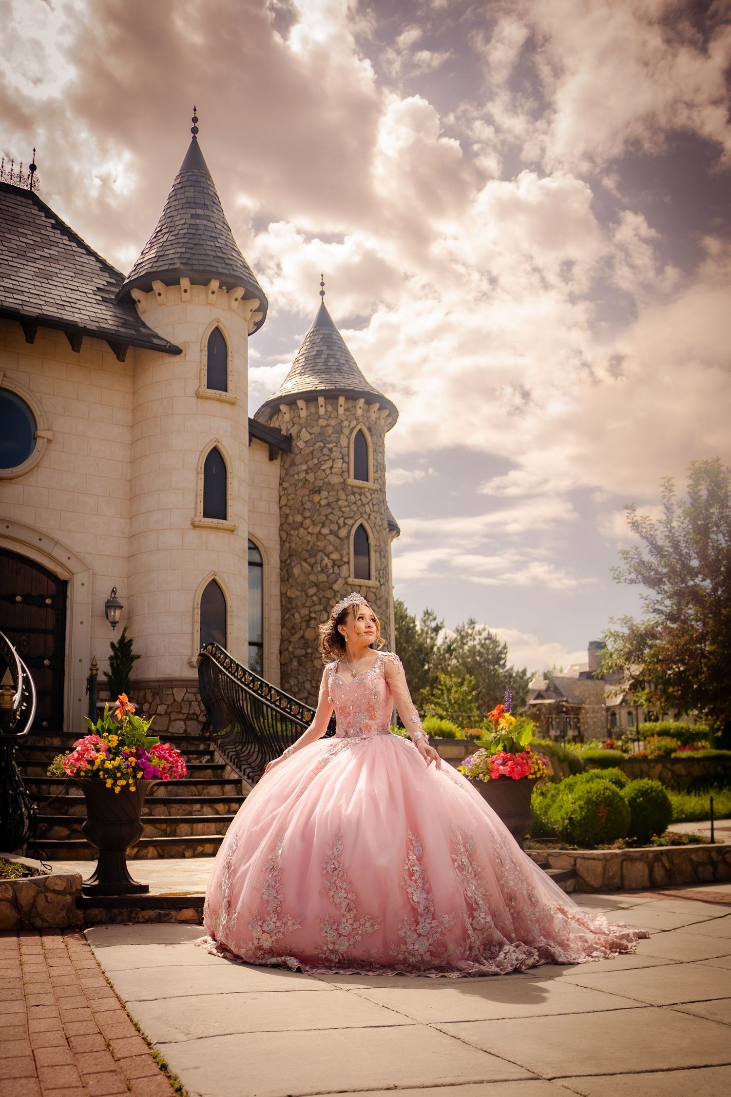 Young woman in a pink ball gown quinceañera dress posing in front of a castle-style venue.