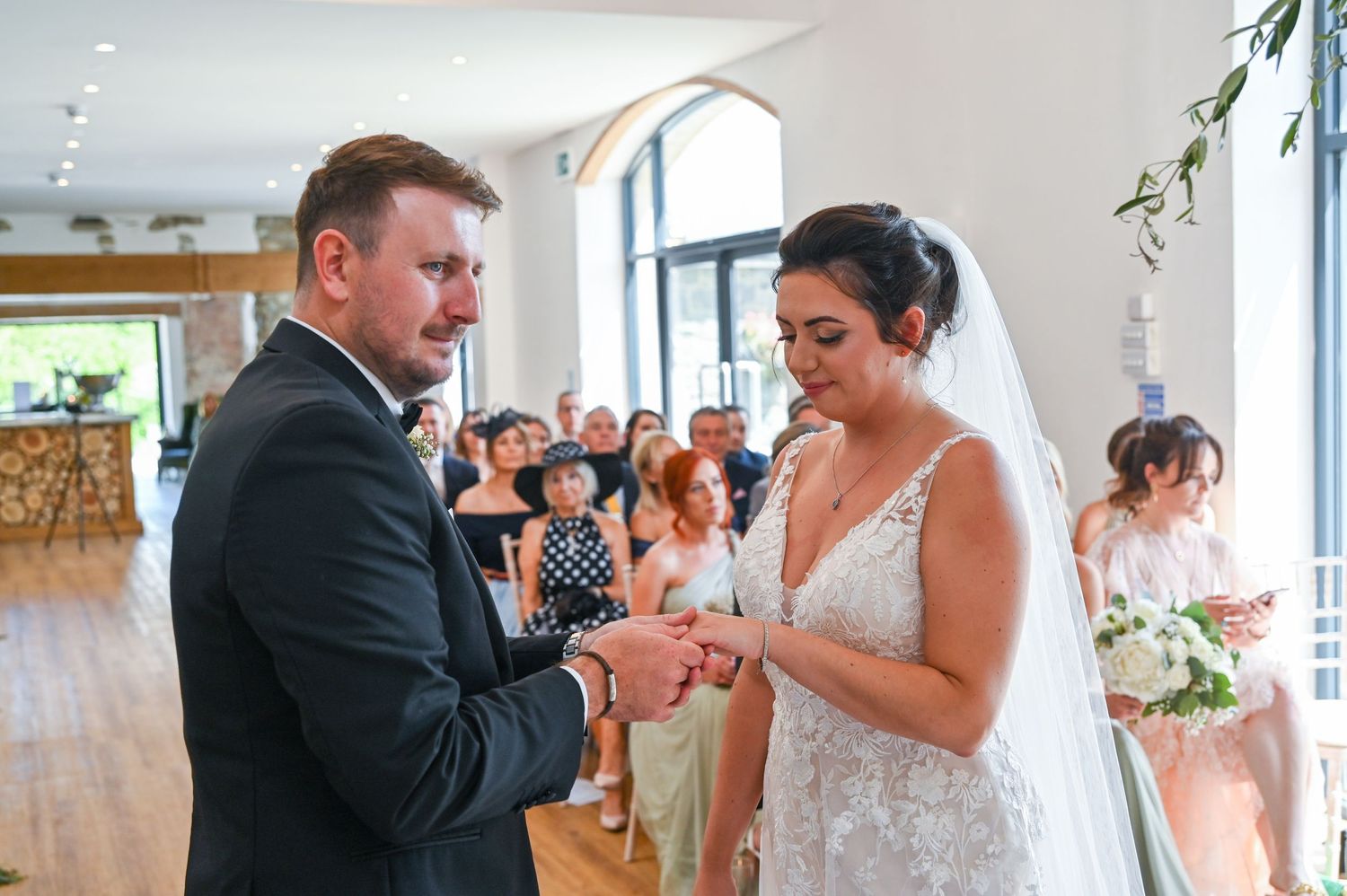 Exchange of rings during wedding ceremony in bright reception hall.