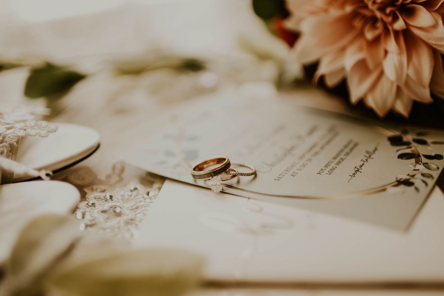 Wedding details with rings and invitation cards in soft vintage lighting.