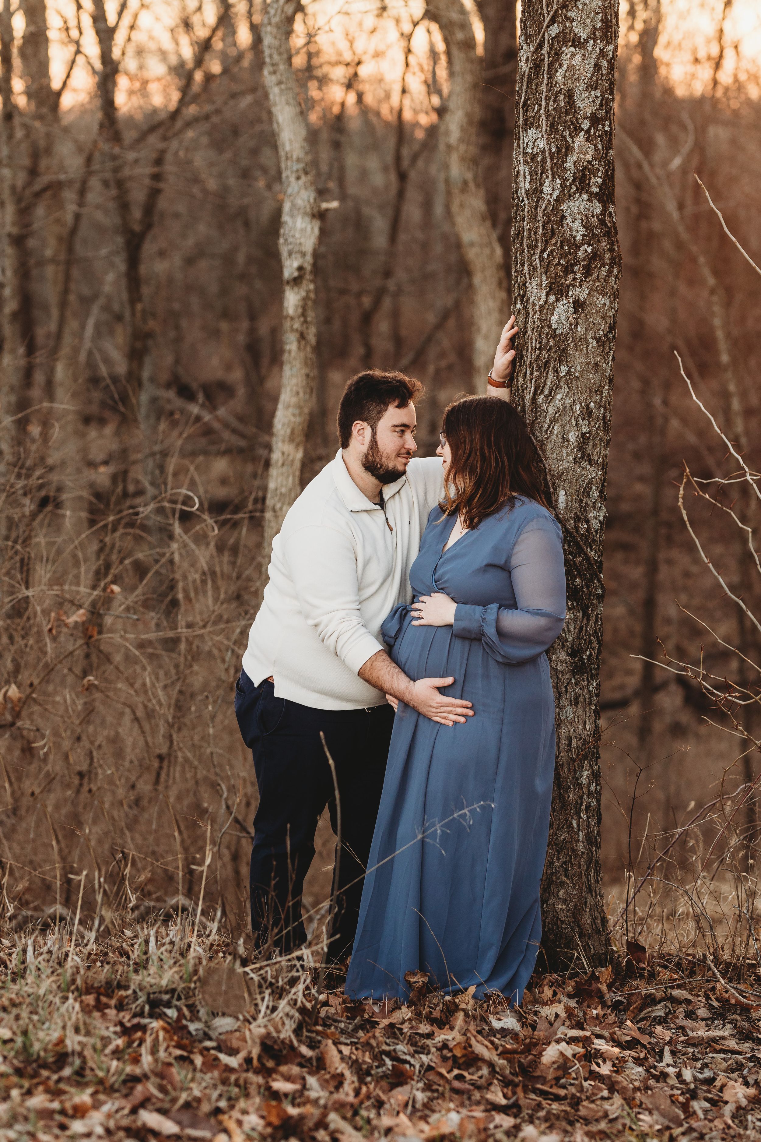 Romantic maternity photo of couple in woods at sunset.