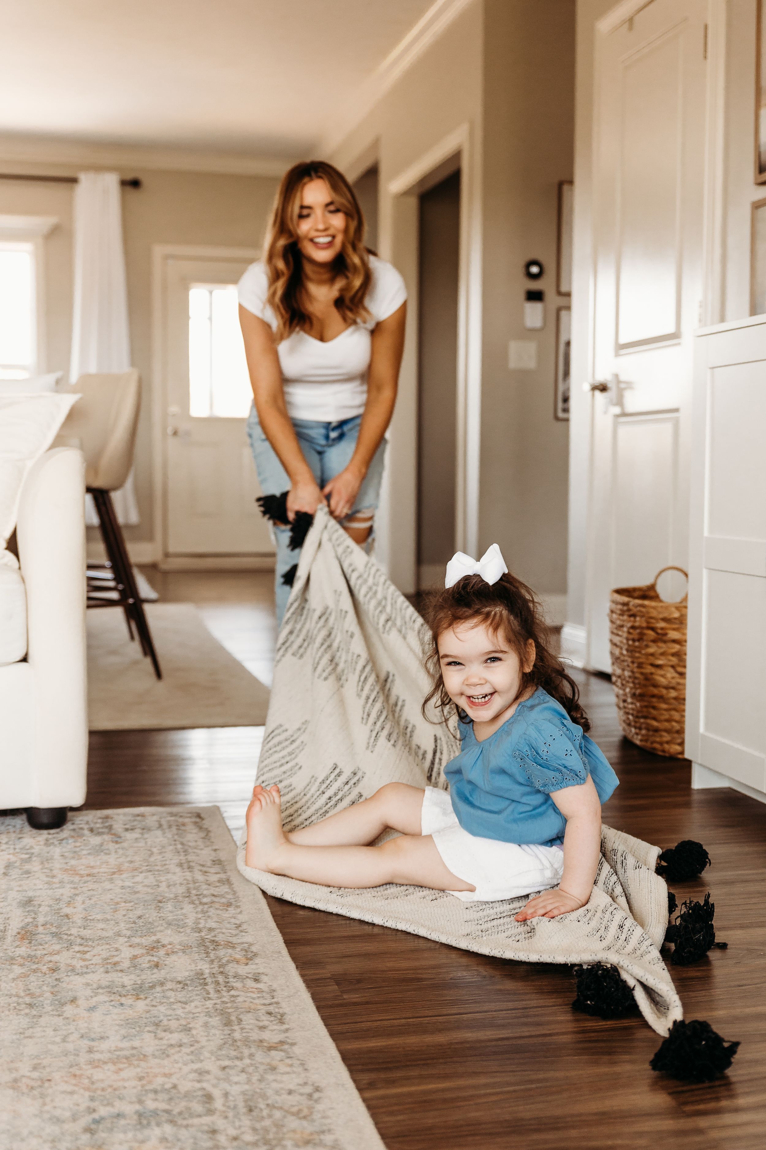 Playful indoor scene with child being pulled across hardwood floor on blanket.