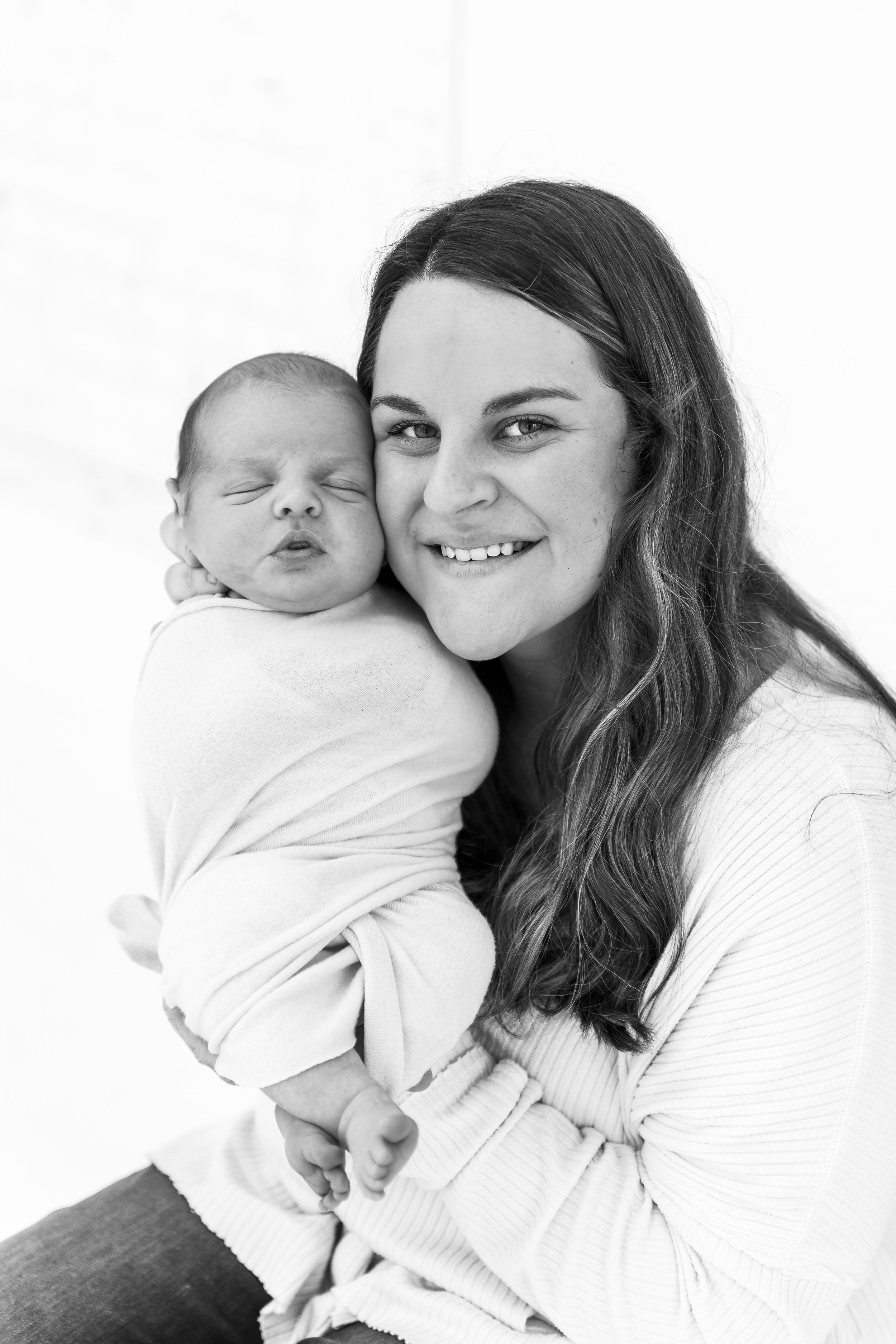 Black and white portrait of mother and newborn baby in matching white outfits.