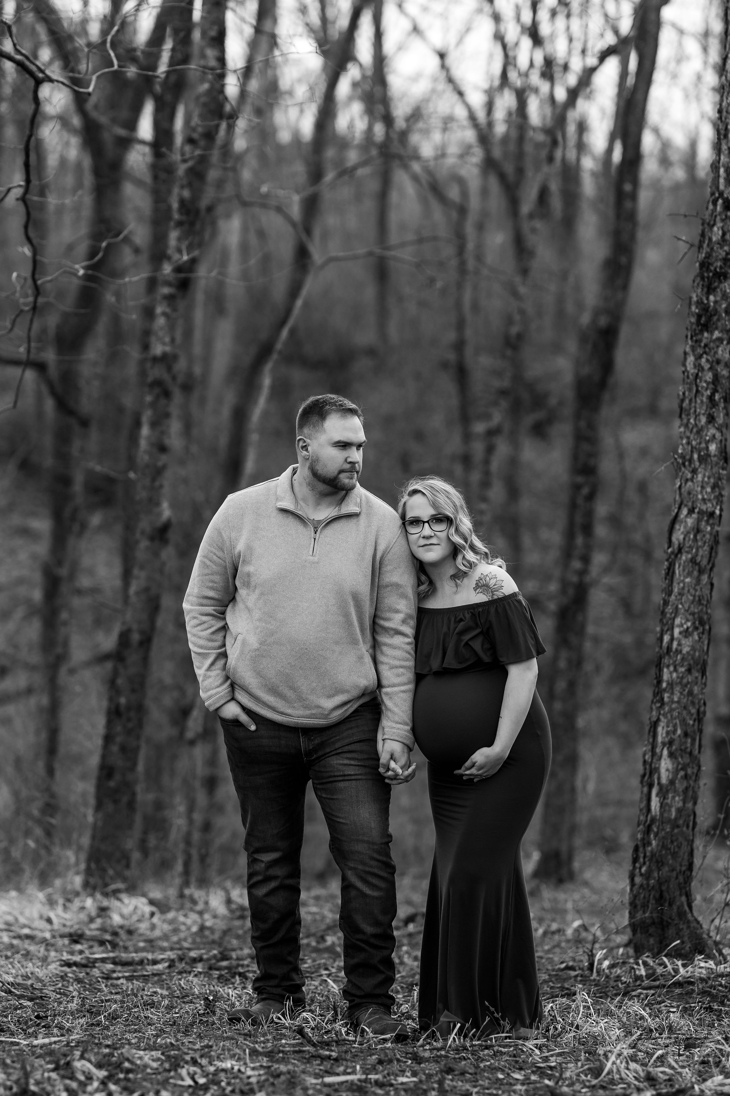 Expecting couple holding hands in winter forest setting.
