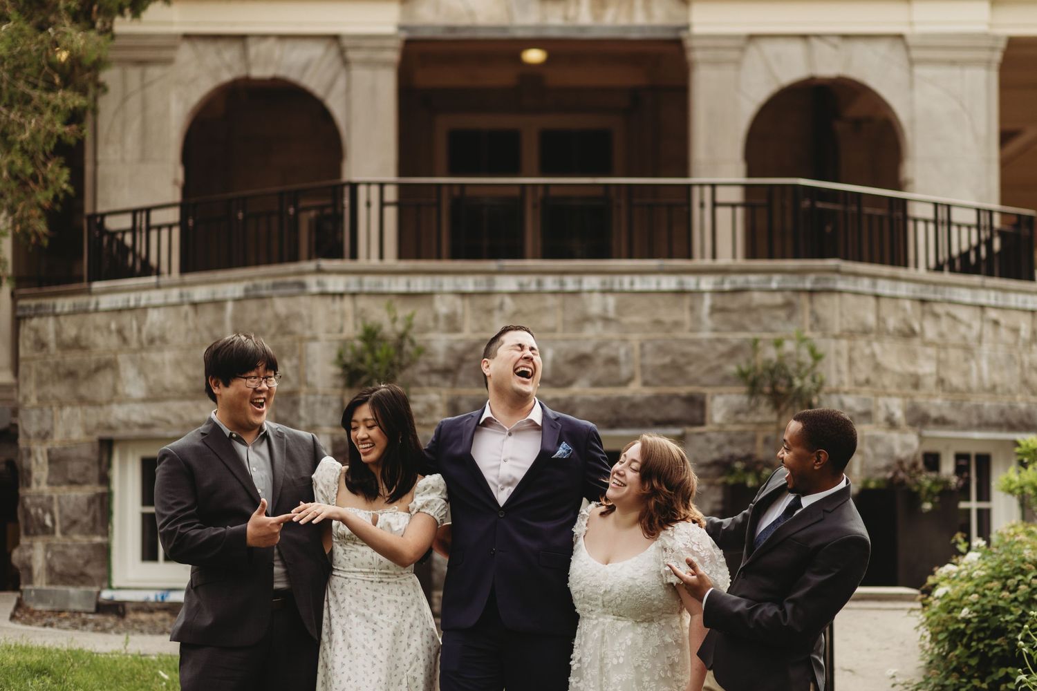 Wedding party sharing a lighthearted moment on a stone balcony.