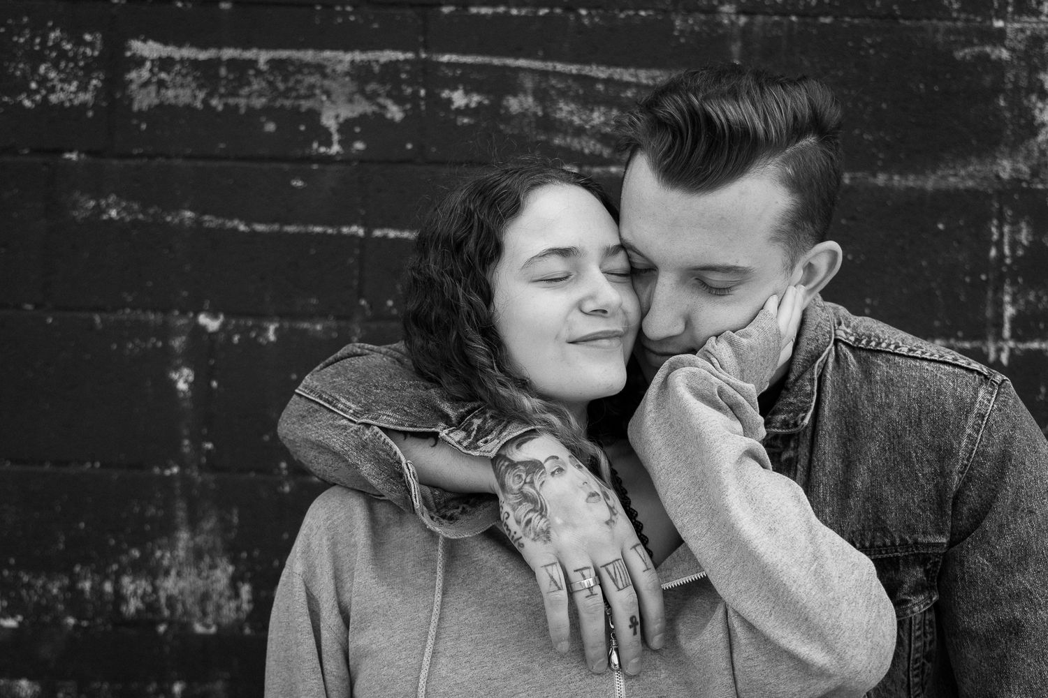 A man has his arm around his girlfriend as she snuggles into his cheek, her hand on his other cheek.