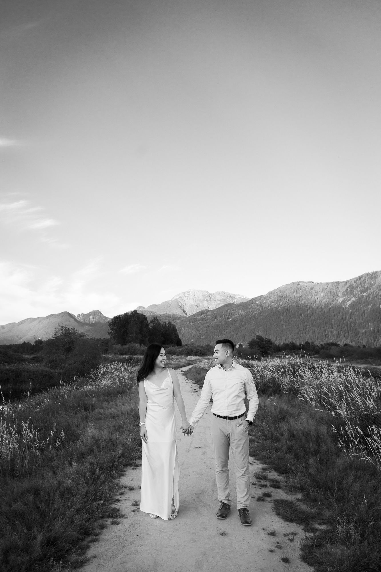 A couple holds hands, looking at each other, the mountains are beautiful behind them.