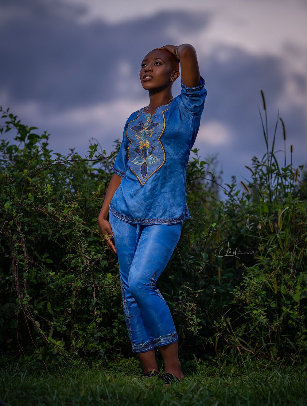 Outdoor fashion portrait of woman in blue traditional outfit against cloudy sky.