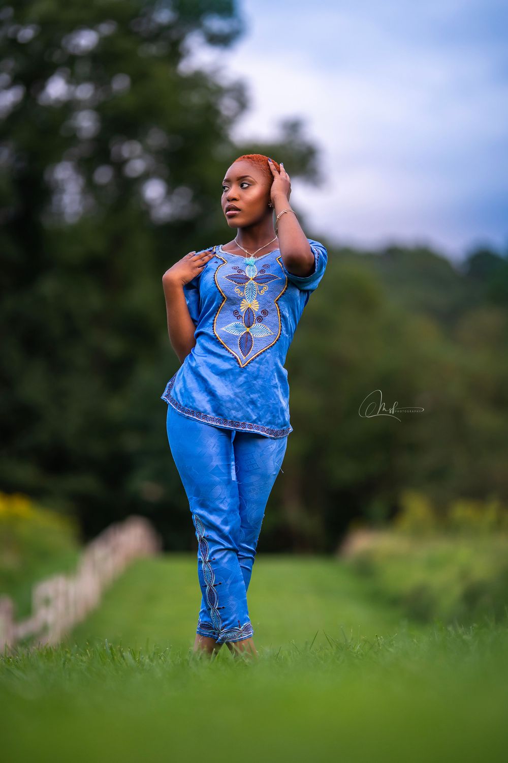 Woman in matching blue embellished outfit poses gracefully in green field.