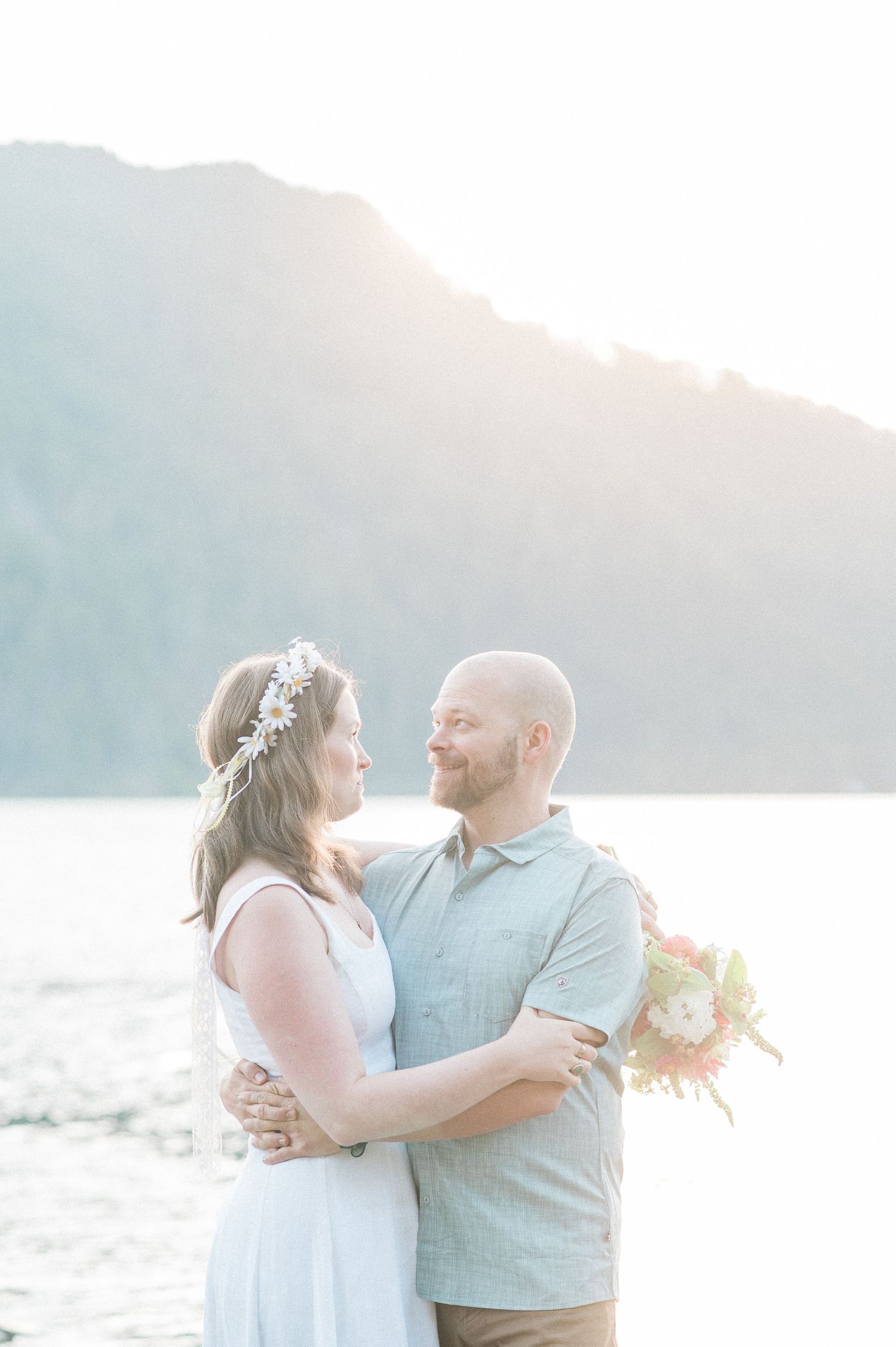 couple embraces together with sunrise behind them and blue mountain