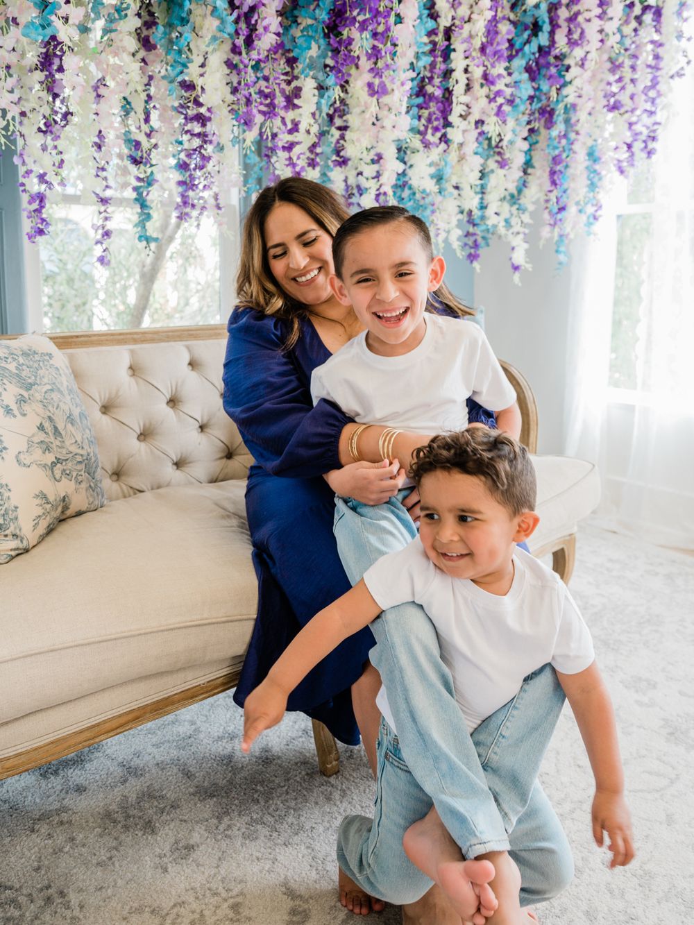 A playful family moment captured under hanging purple and blue floral decorations on a tufted couch.
