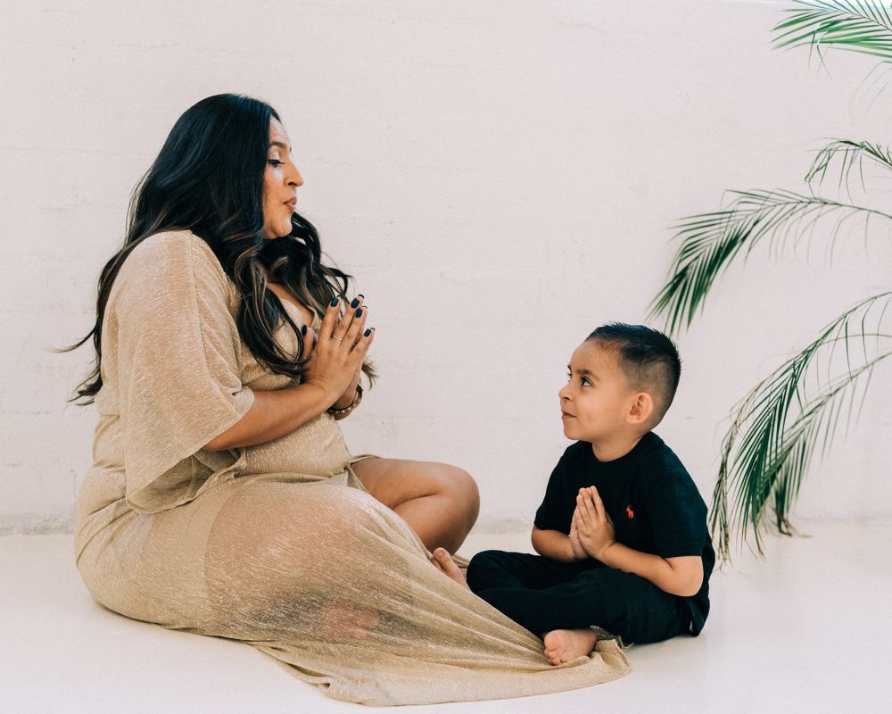 A playful parent and child moment sitting on a light-colored floor with palm plants in the background.