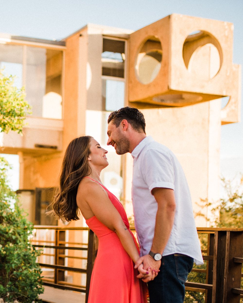 Couple shares romantic moment in front of modern architectural building with circular windows.