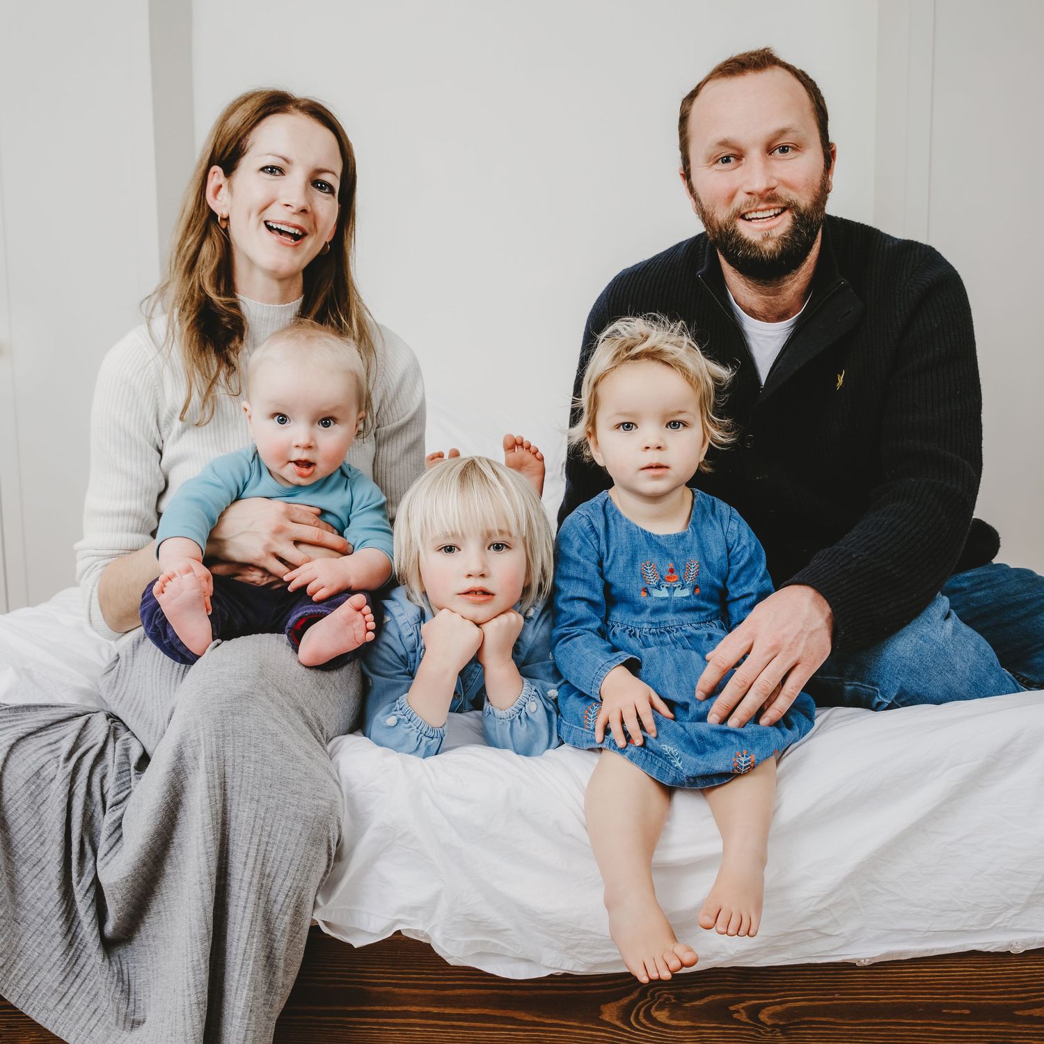 Family portrait with parents and three young children sitting together on white bedding, in Stoke Newington.