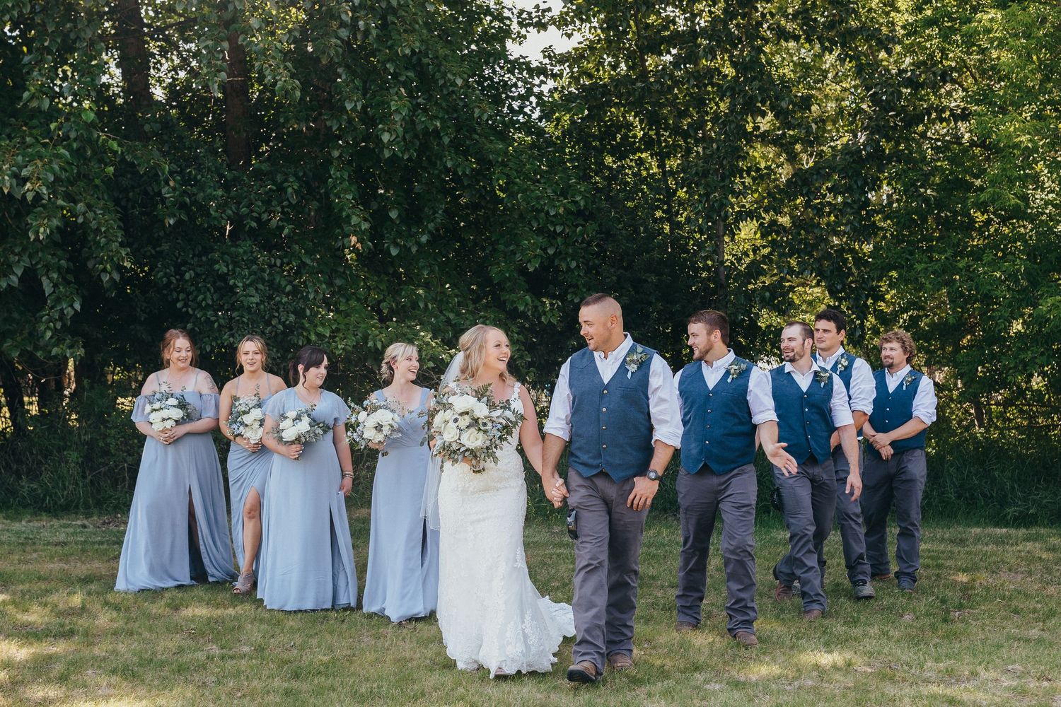 Wedding party lined up outdoors with bridesmaids in light blue dresses and groomsmen in navy vests.