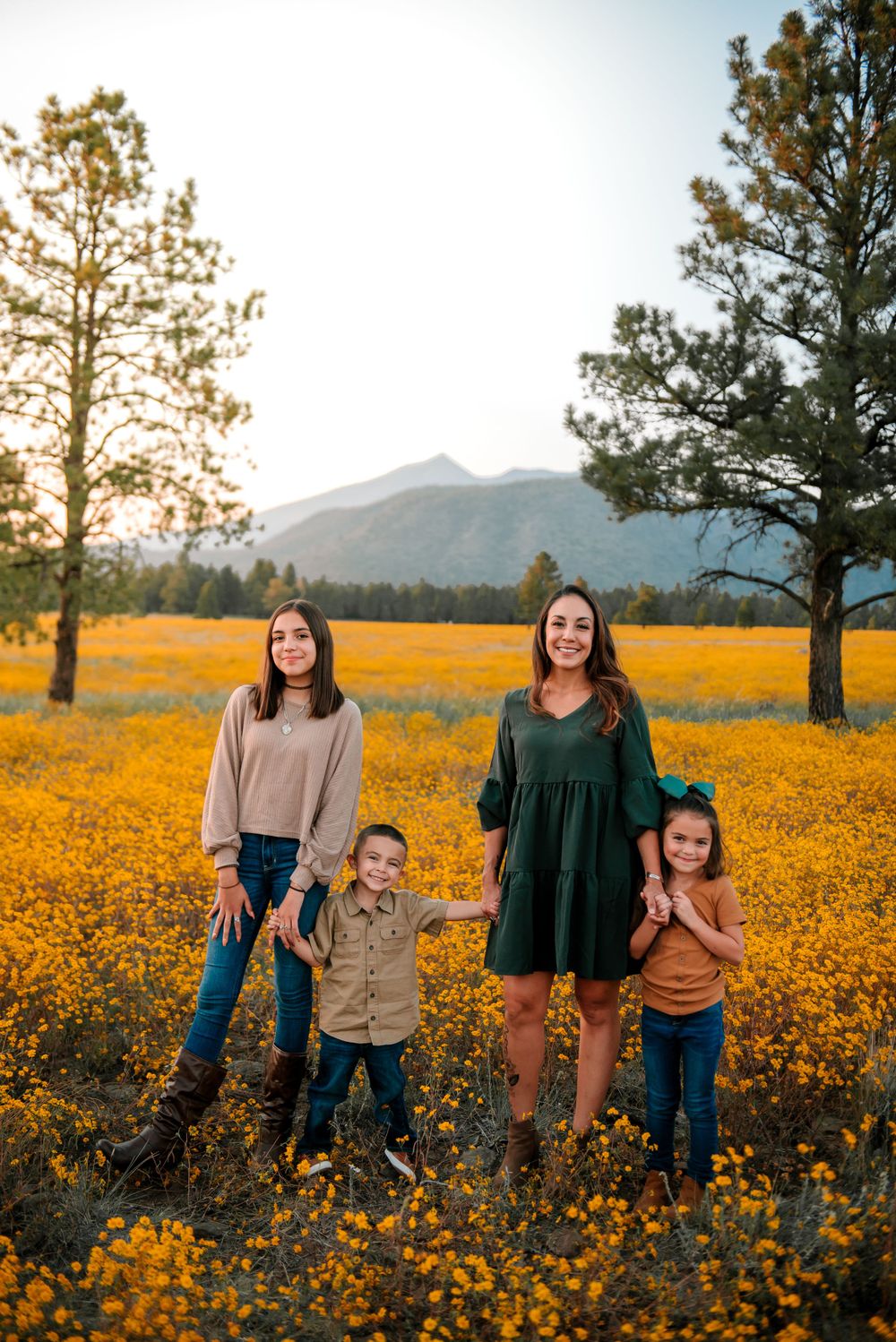 Family portrait in field of yellow wildflowers with mountain landscape at sunset.
