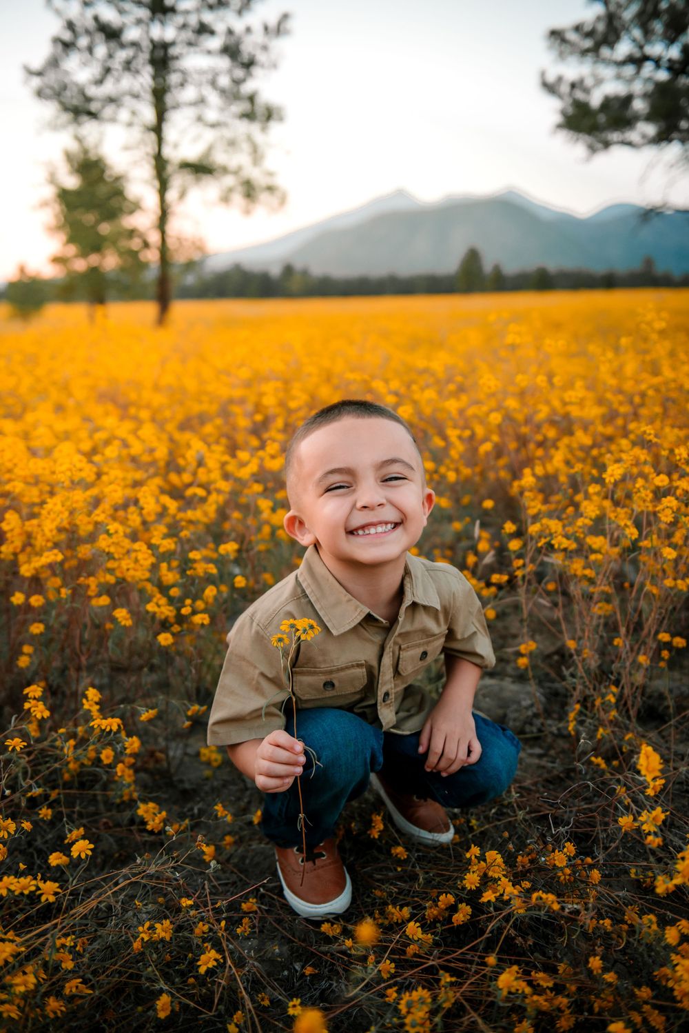 A joyful moment captured in a vibrant field of yellow wildflowers at sunset with mountains in the background.