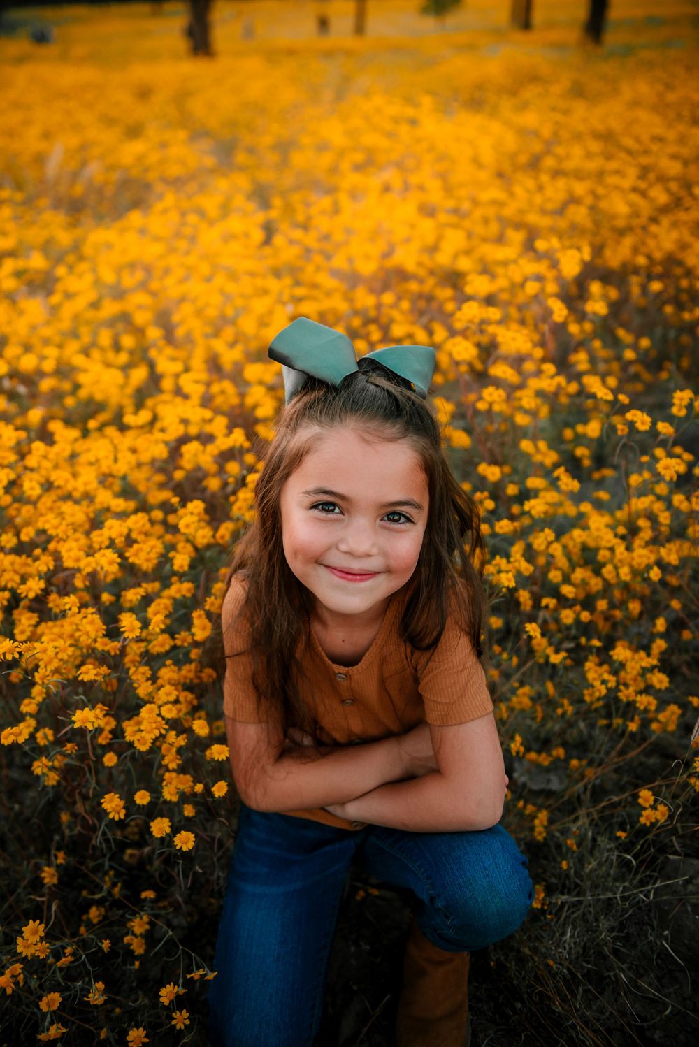 Girl with teal bow smiling in a field of golden wildflowers during sunset.
