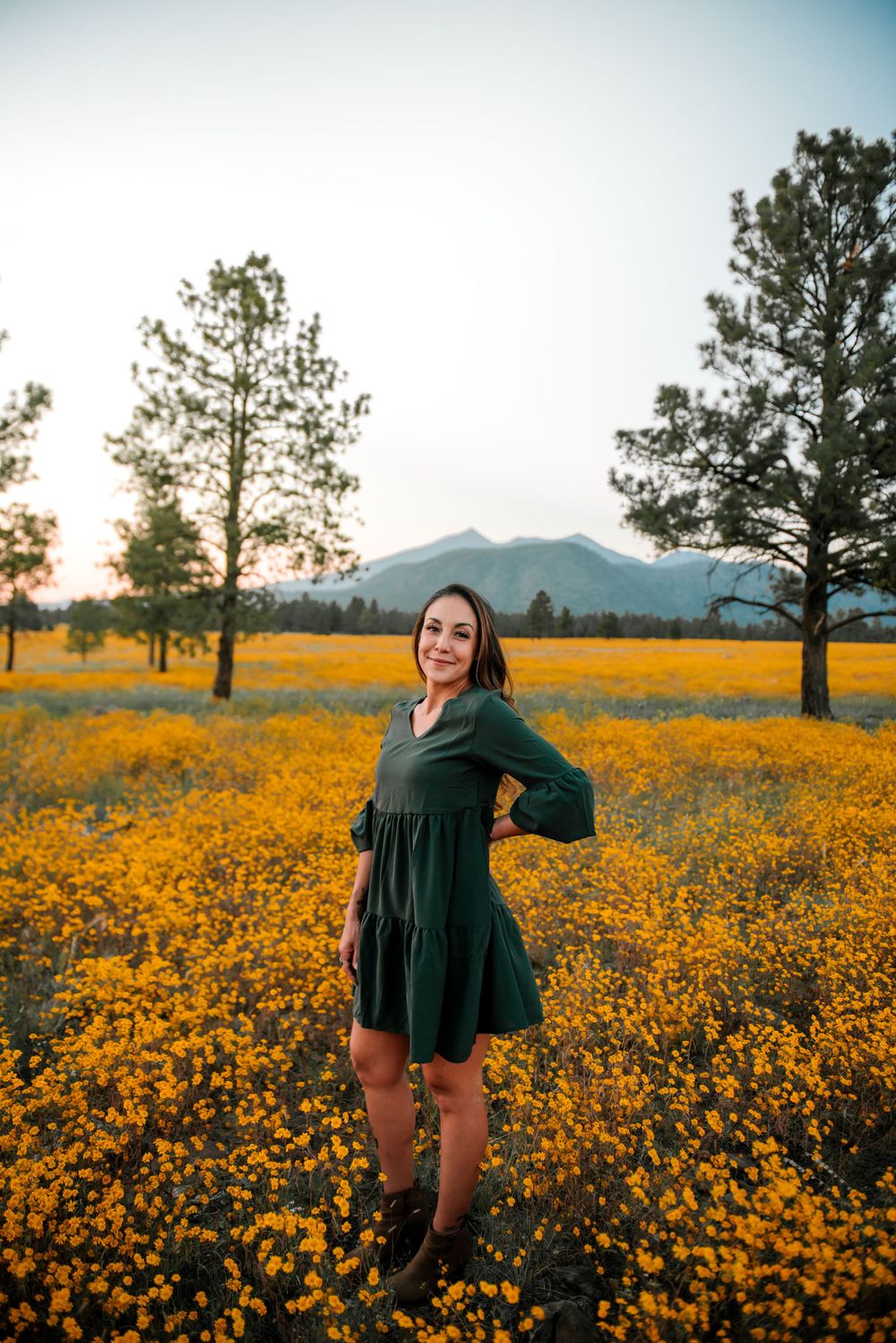 Woman in a dark dress twirls through a field of golden wildflowers with mountains in the distance.