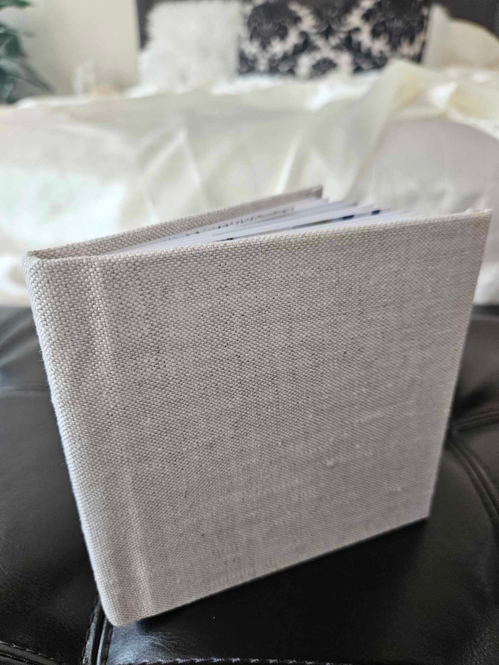 Gray linen photo album displayed on dark leather surface.