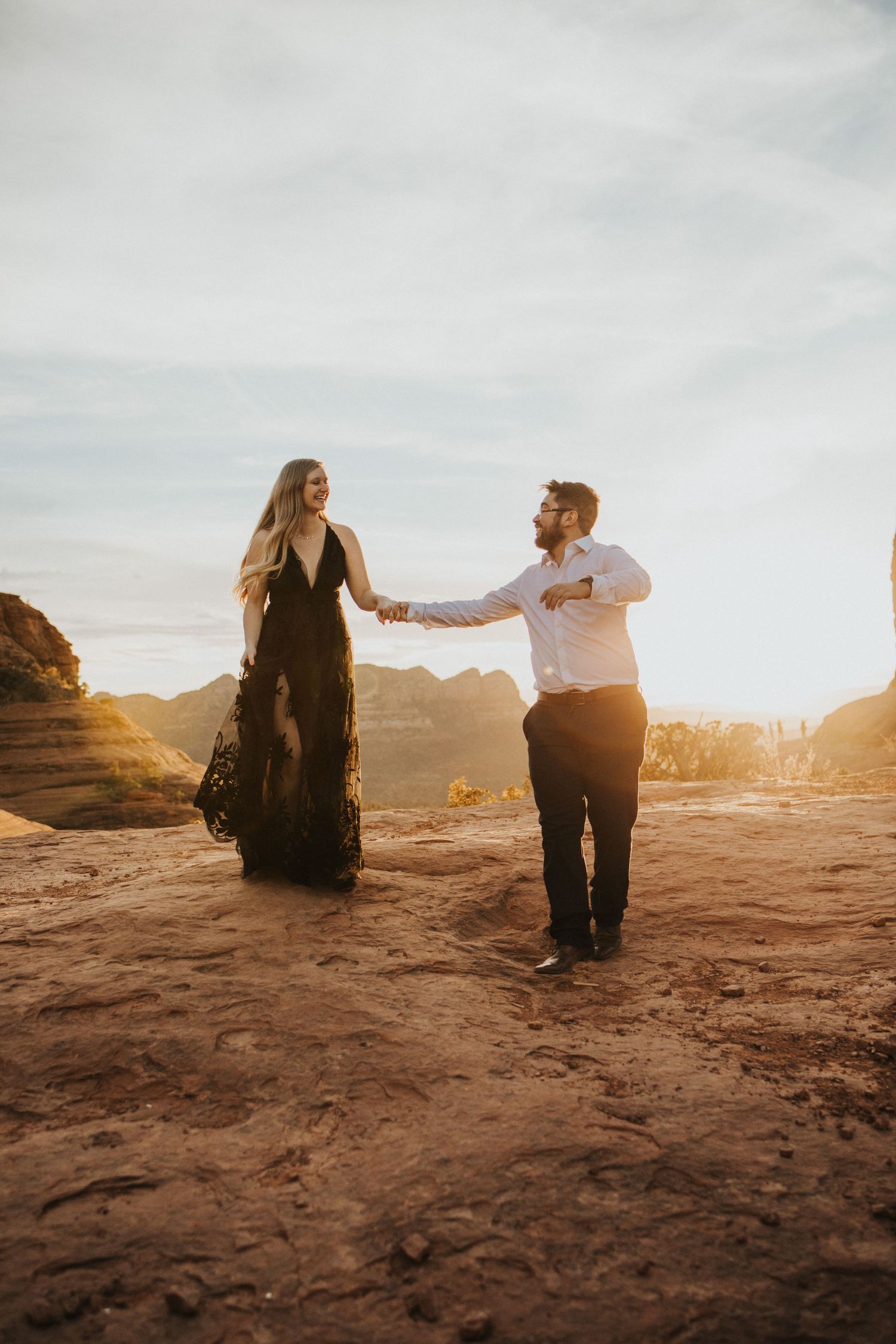 Engaged couple running across red rocks in sedona with beautiful mountains in the back