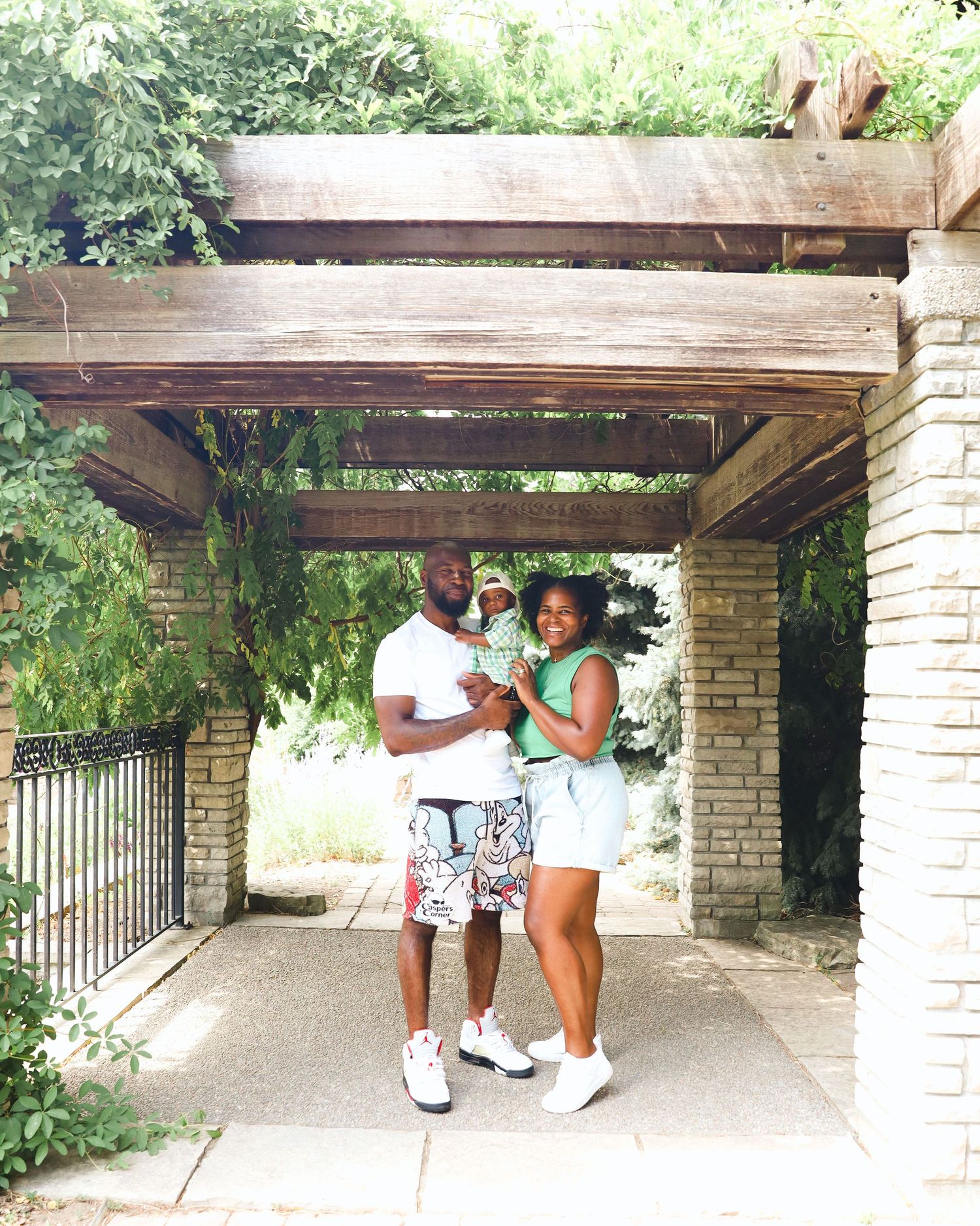 Couple poses together under a rustic wooden pergola on a sunny day.