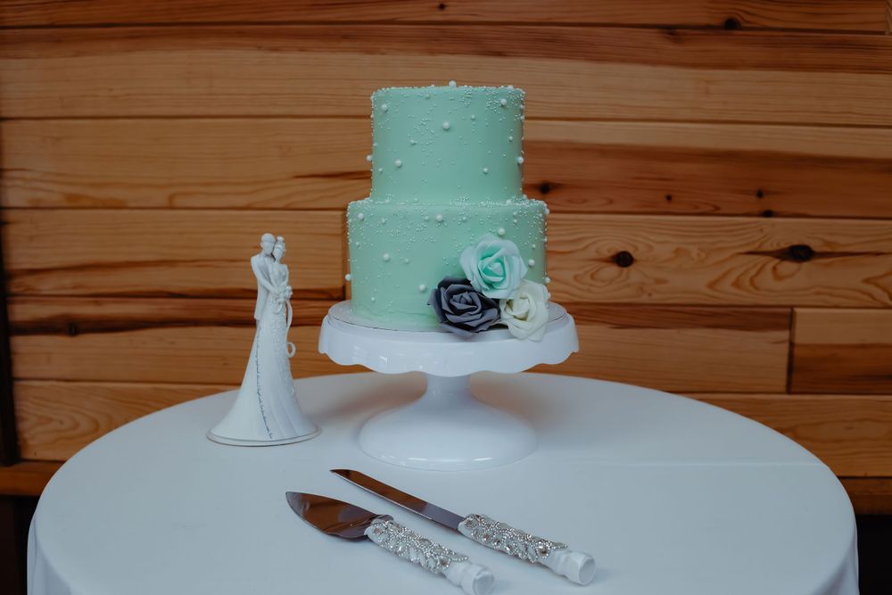 Mint green wedding cake with navy blue roses on a white cake stand next to serving utensils.