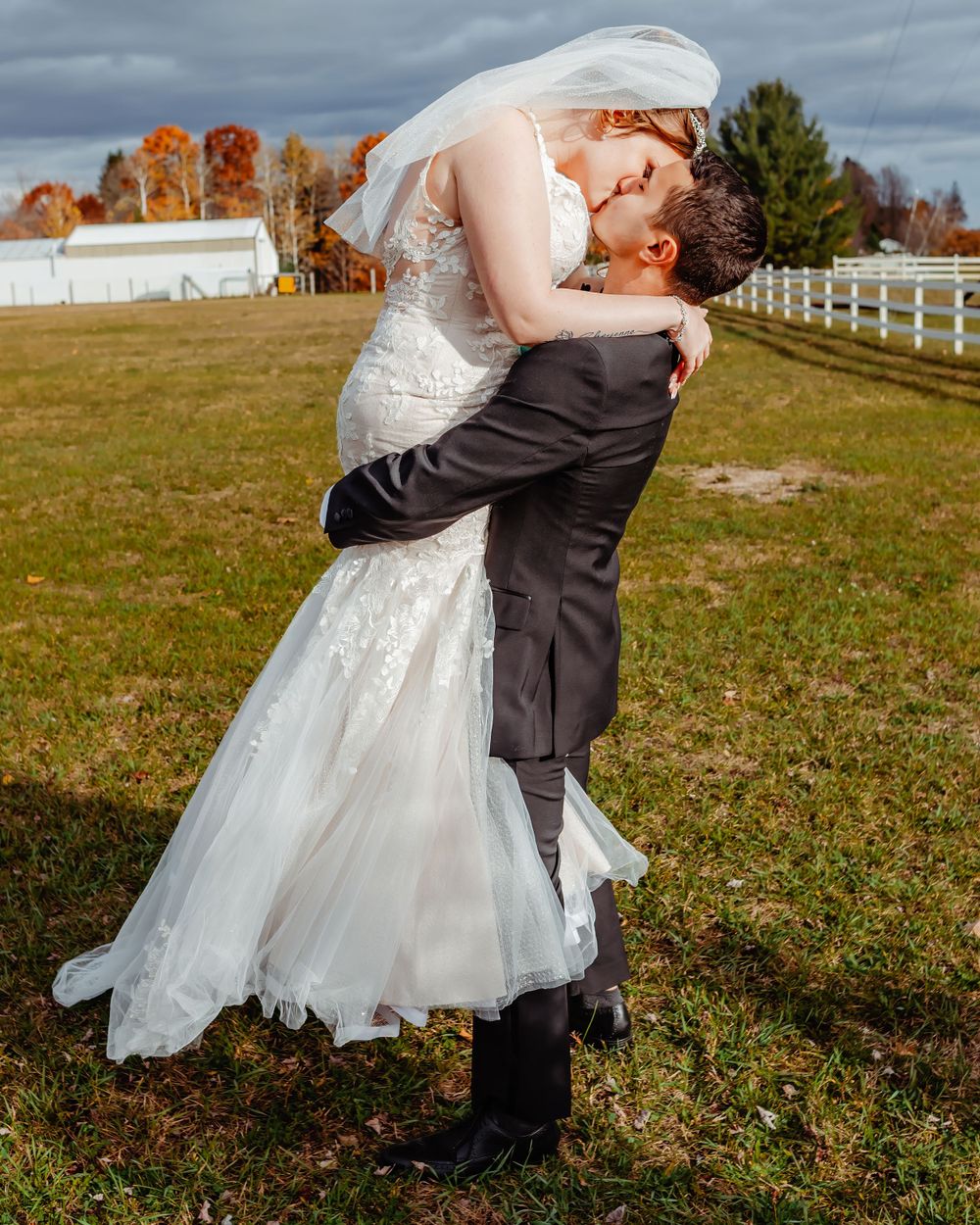 Romantic wedding couple embracing on autumn farm grounds with white fence.