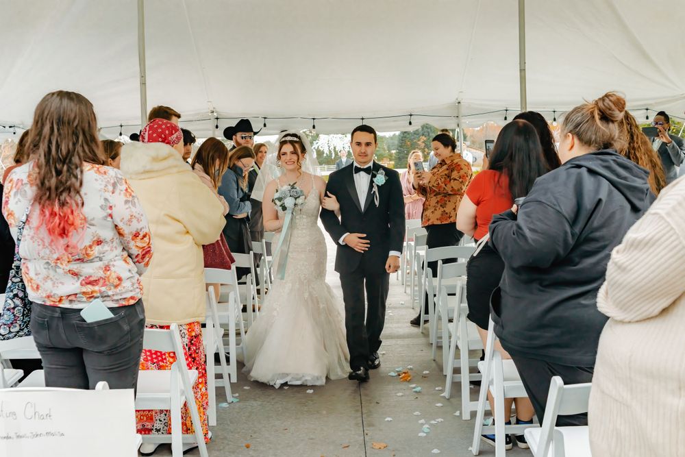 Wedding ceremony procession in a white tent with rows of chairs.