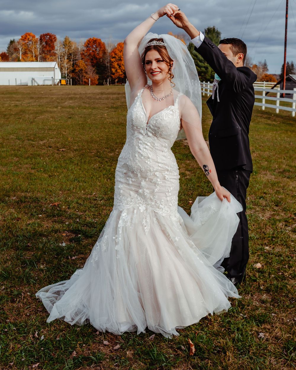 Dancing couple in wedding attire on farm grounds with autumn foliage.