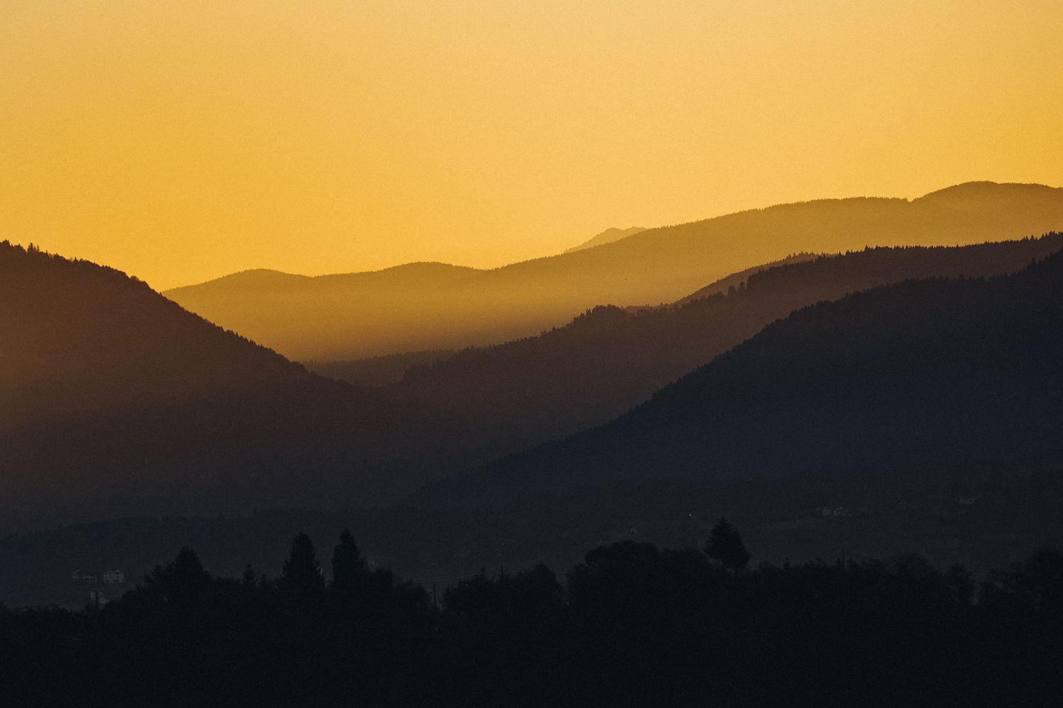 Silhouetted mountain ranges at sunset creating layered shadows against a golden sky.