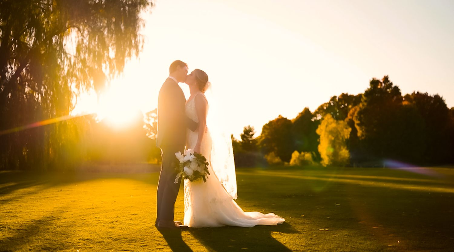 Wedding couple silhouetted against golden sunset on a golf course.