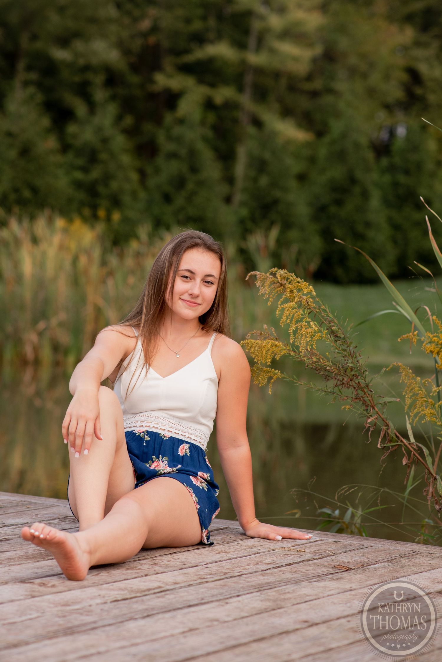 A casual portrait on a lakeside dock with natural scenery and golden cattails in the background.