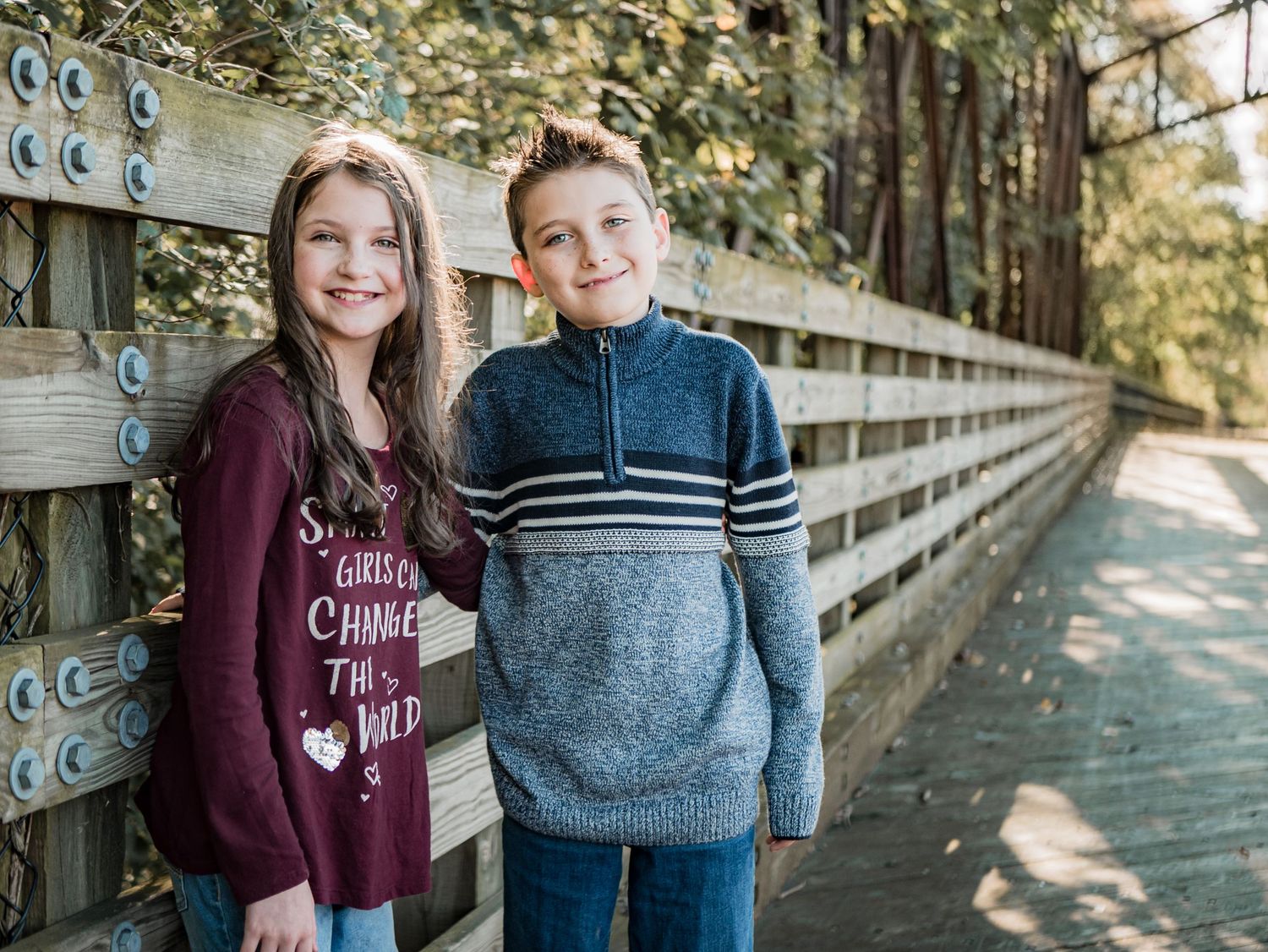 Two young people pose together on wooden bridge wearing casual sweaters.