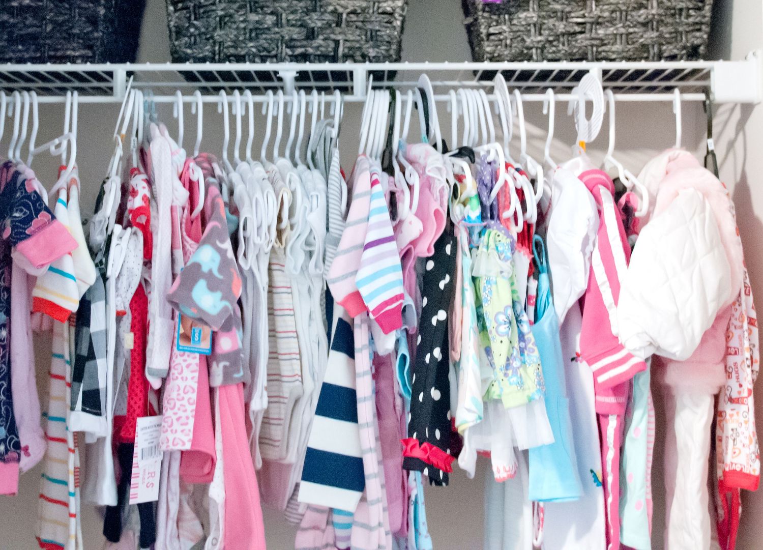 Organized baby clothes closet with pink and blue garments hanging neatly on white hangers.