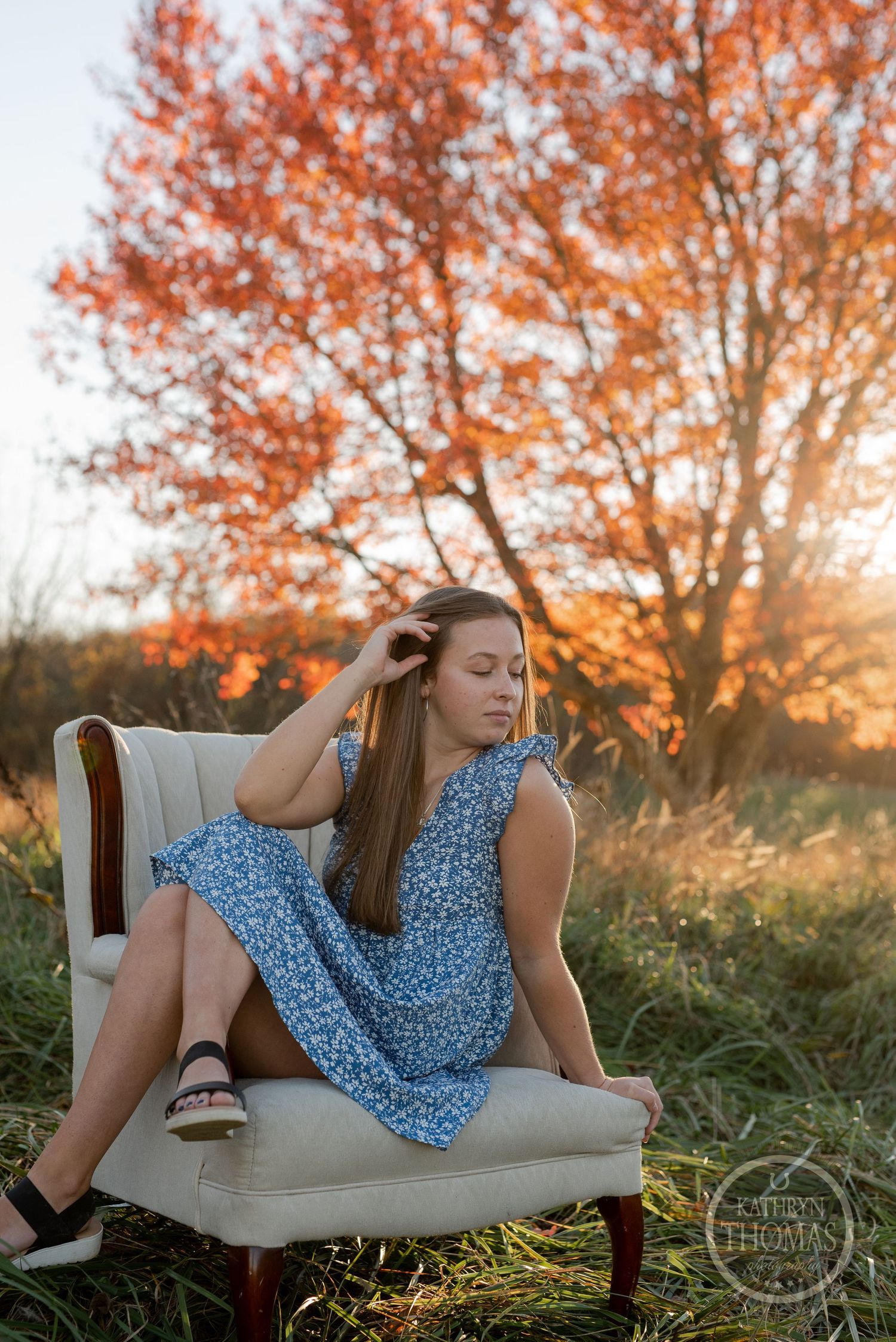 A blue floral dress on a vintage chair with autumn trees glowing in the sunset background.