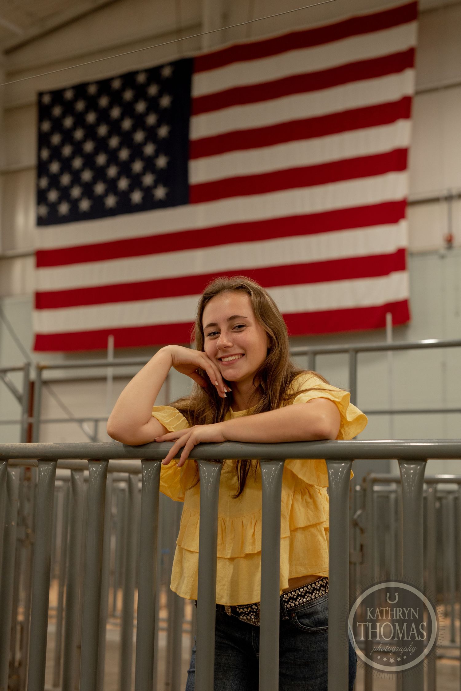 A yellow-shirted person leans casually against a railing with an American flag displayed prominently in the background.