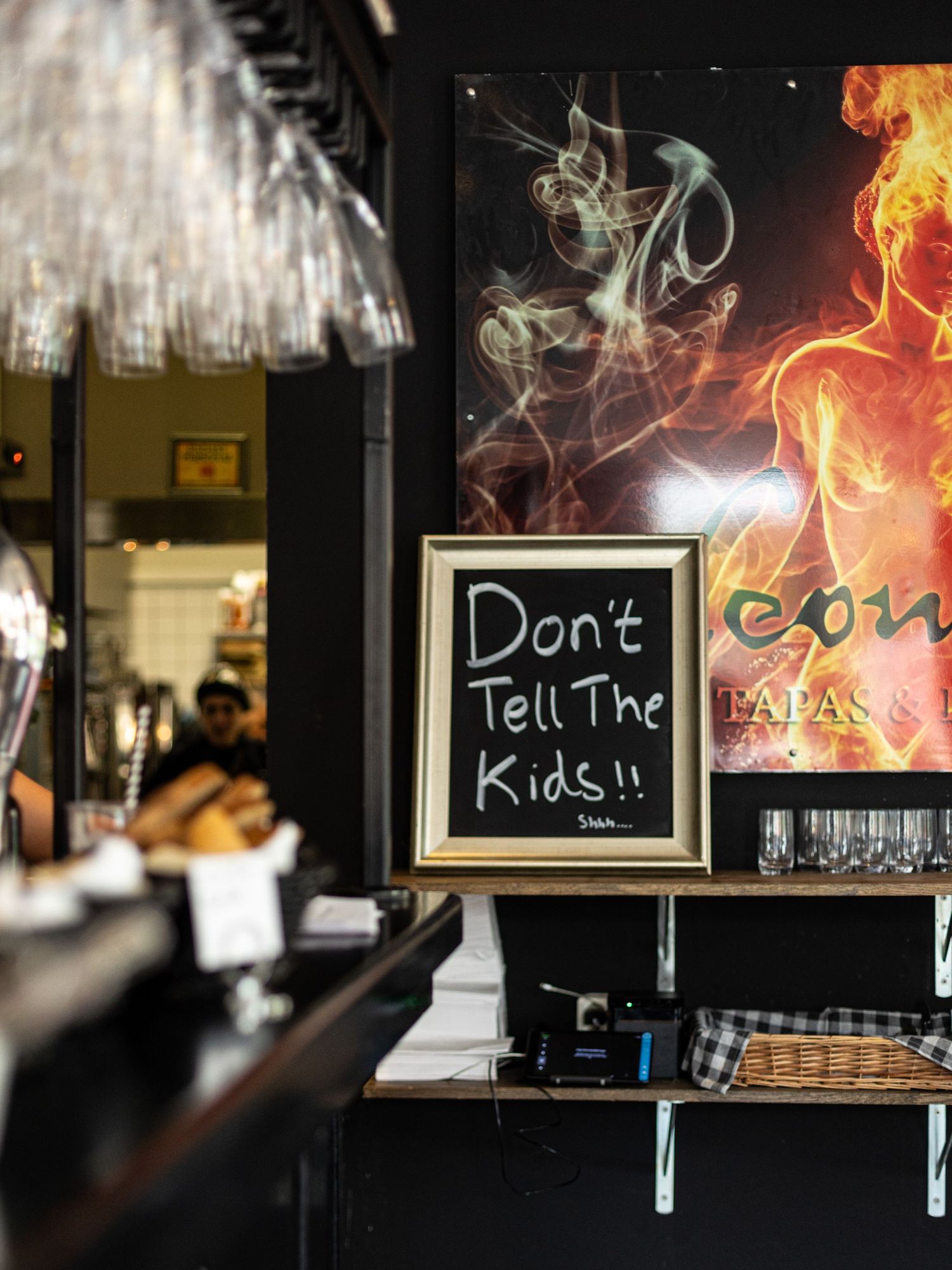 Bar sign reading 'Don't Tell The Kids' with smoke and fire artwork in background.