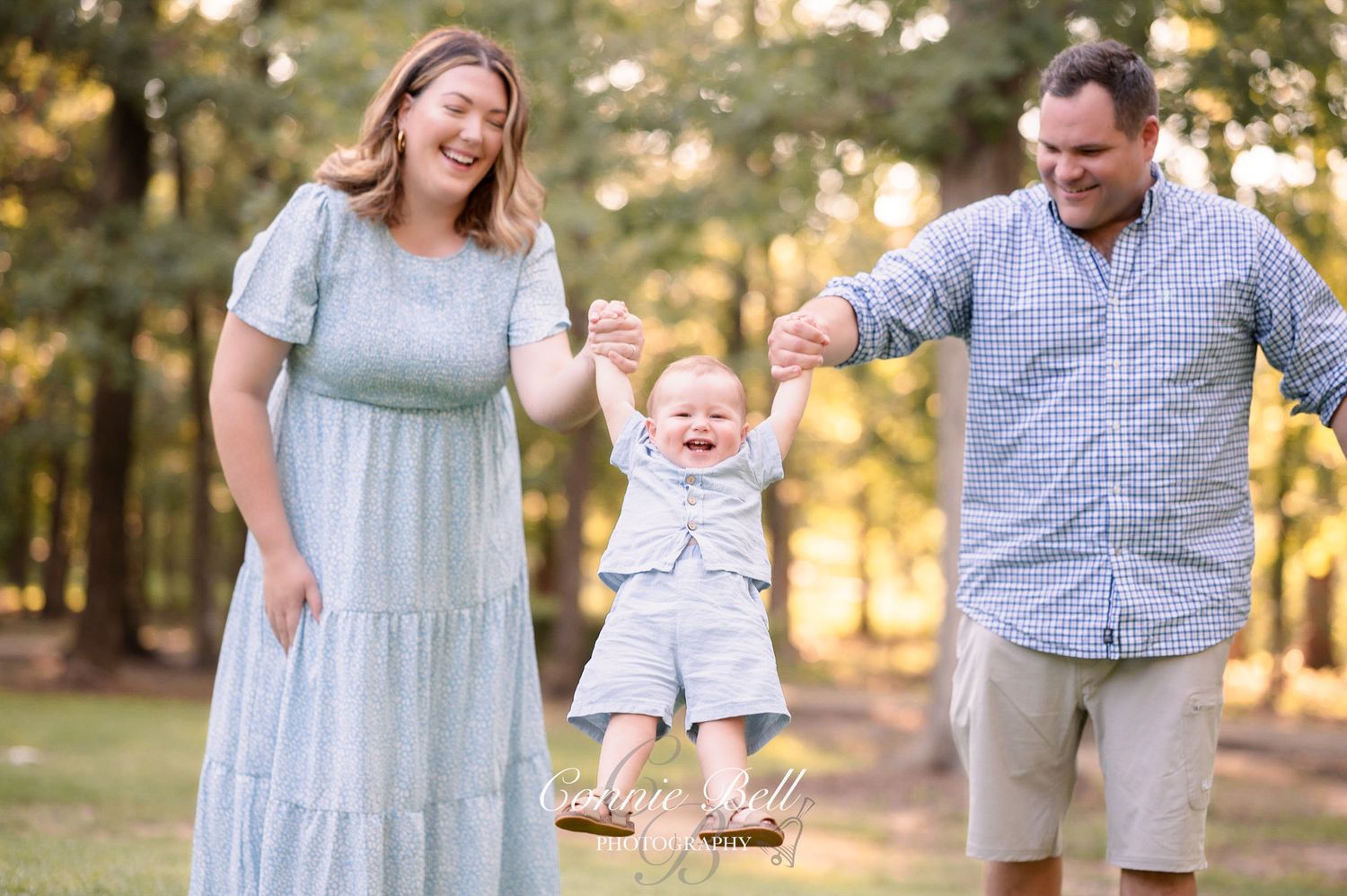 Family swings delighted baby in summer evening outdoor portrait session.
