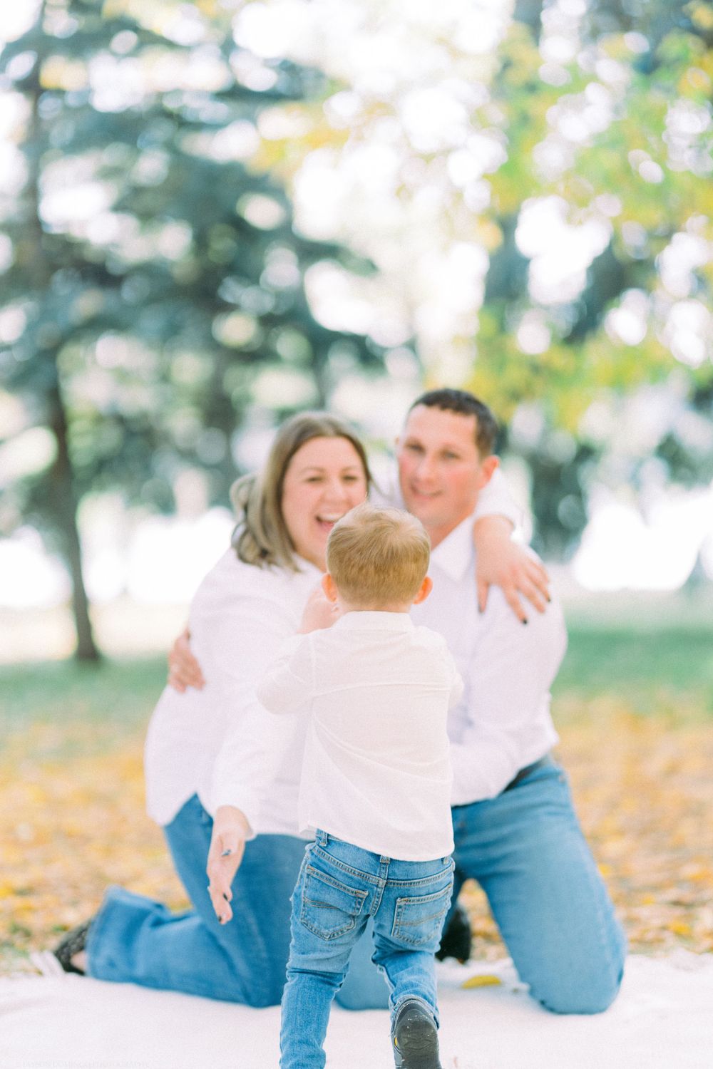 Family in white shirts and jeans playing together on autumn ground.
