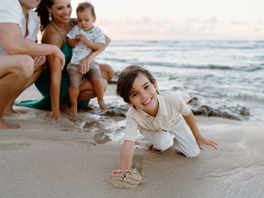 A family photoshoot by Moments With Kell on Oahu in Hawaii with parents and child playing on the sand