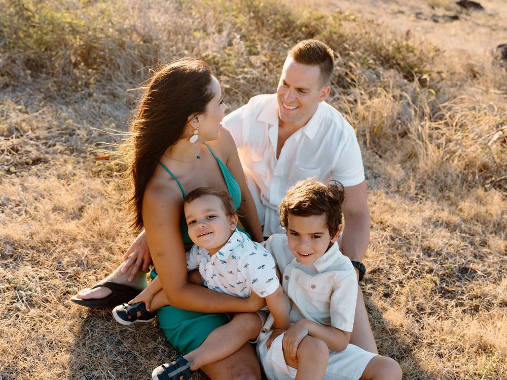 A family photoshoot by Moments With Kell with a grass backdrop on Oahu in Hawaii with parents and children sitting