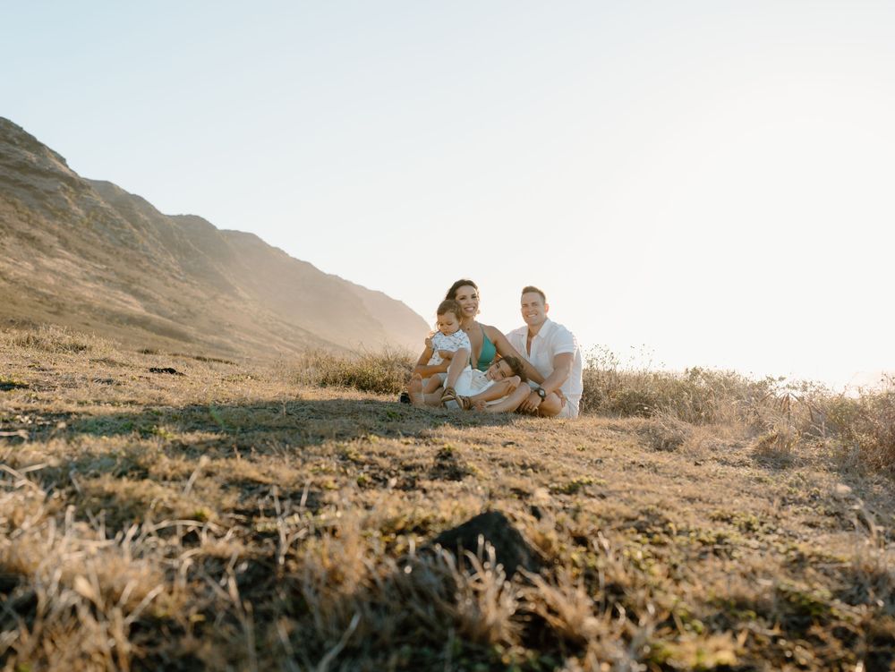 A family photoshoot by Moments With Kell with a mountain backdrop on Oahu in Hawaii with parents and children sitting