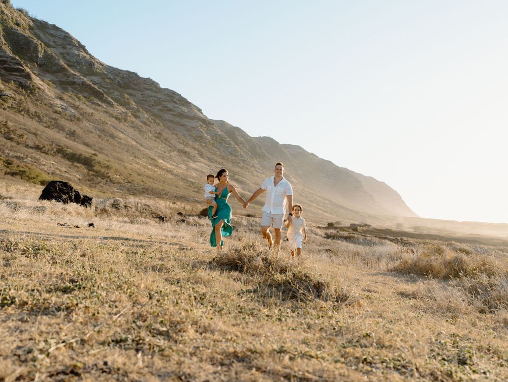 A family photoshoot by Moments With Kell with a mountain backdrop on Oahu in Hawaii with parents and children walking