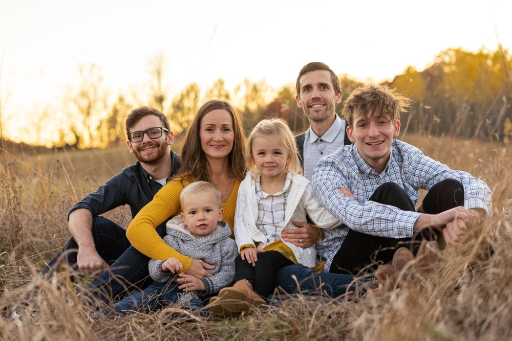 Casual family portrait in tall grass field during golden hour sunset.