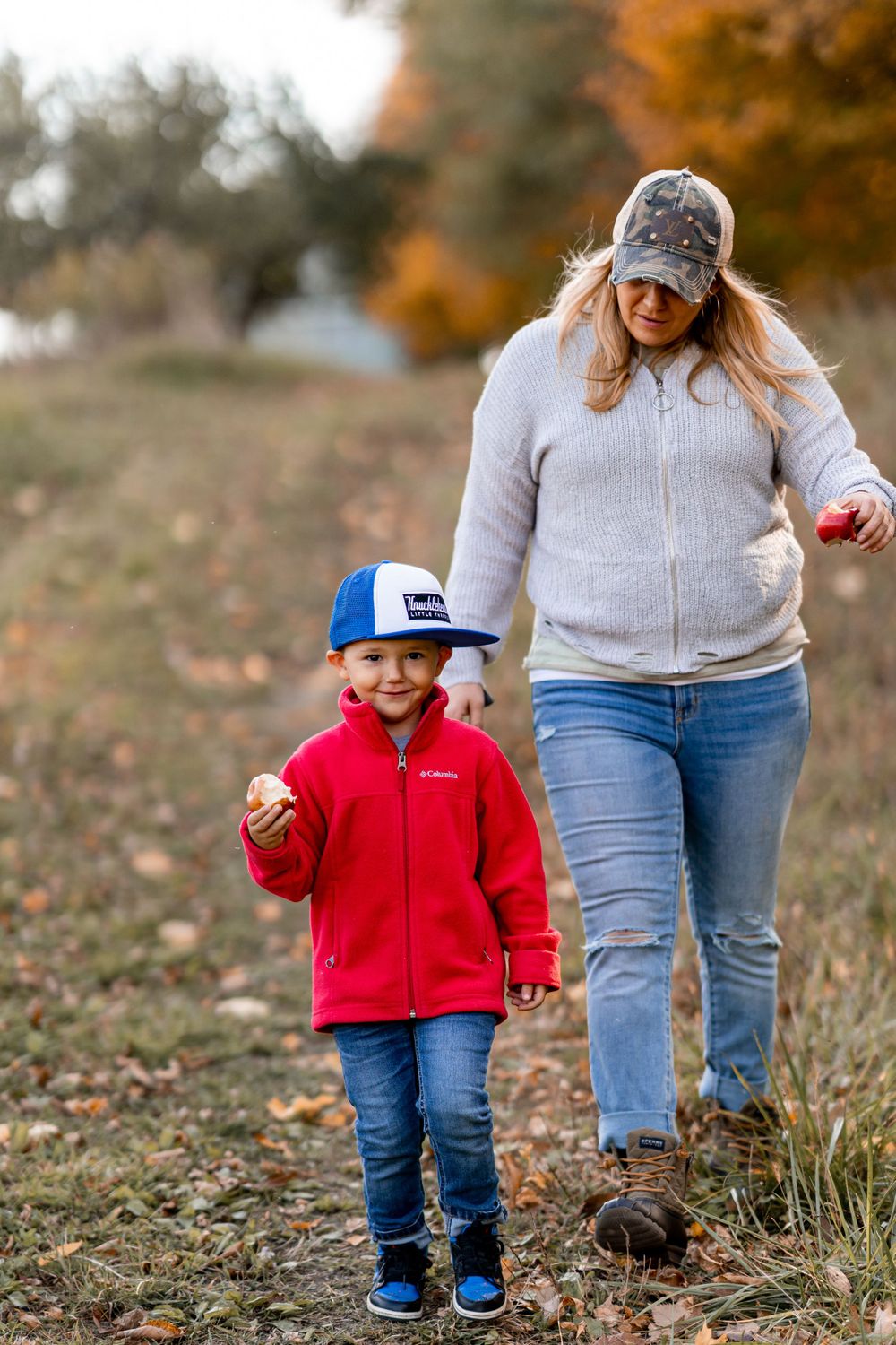 Parent and child walk together on a grassy trail during fall season.